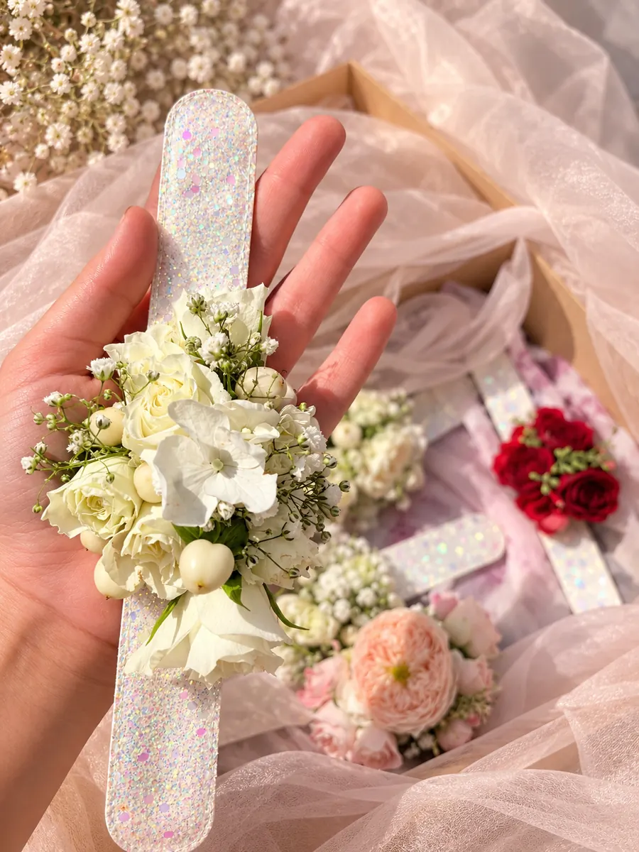 Brățară florală cu flori albe și verdeață, ținută în palmă