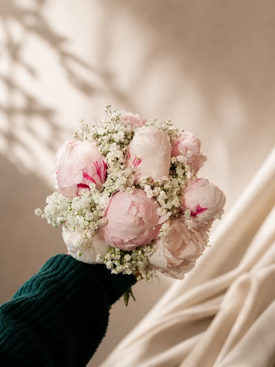 Buchet mic de bujori roz pal și gypsophila, ținut în mână