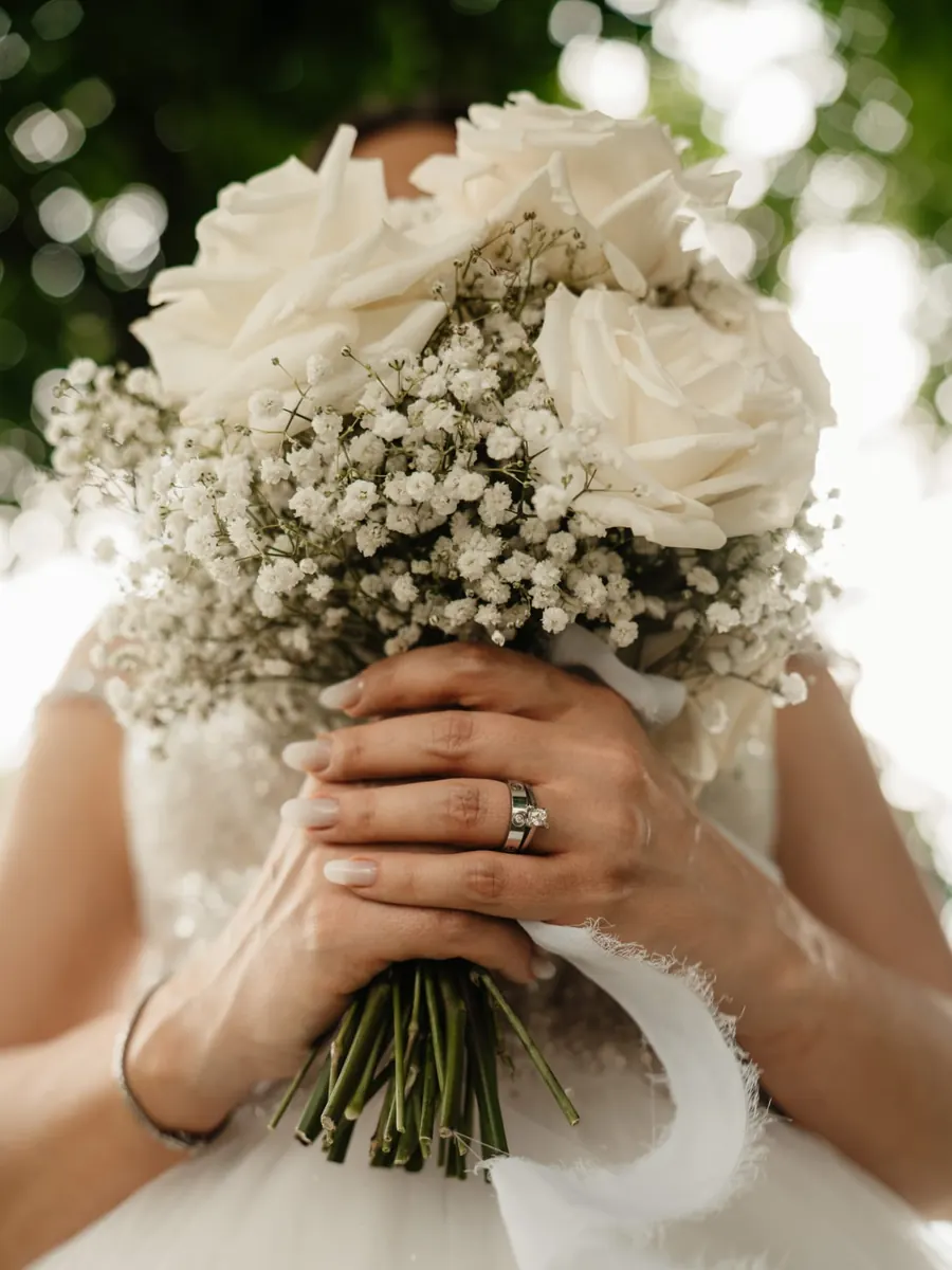 Mireasă ținând un buchet de trandafiri albi și gypsophila, cu inelul la vedere