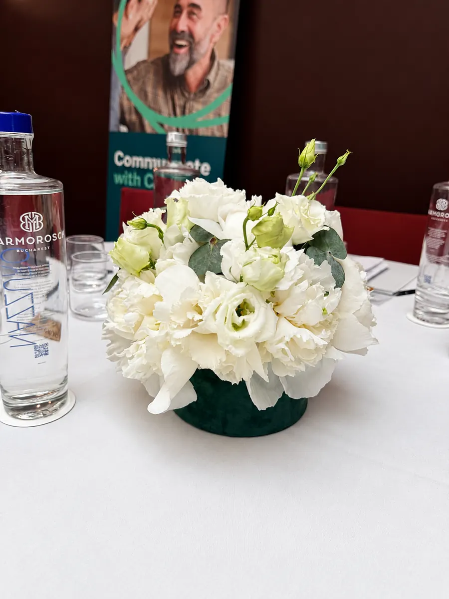 Aranjament cu flori albe pe masa unui eveniment de firmă