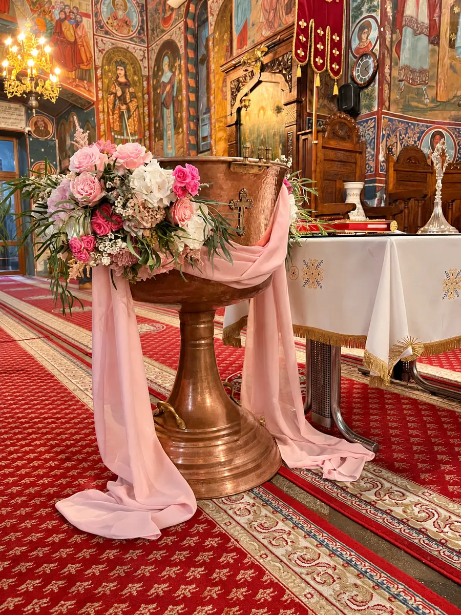 Cristelniță de aramă decorată cu flori roz și voal roz, în biserică