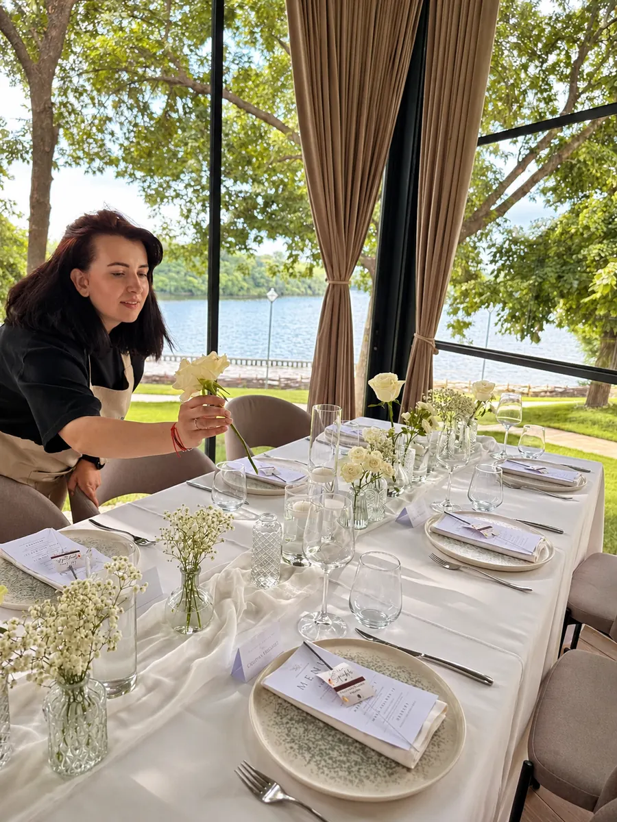 Laura aranjând florile pe masa lungă, lângă lac