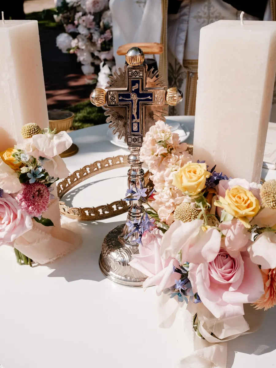 Lumânări de cununie decorate cu trandafiri roz și piersică, lângă cruce
