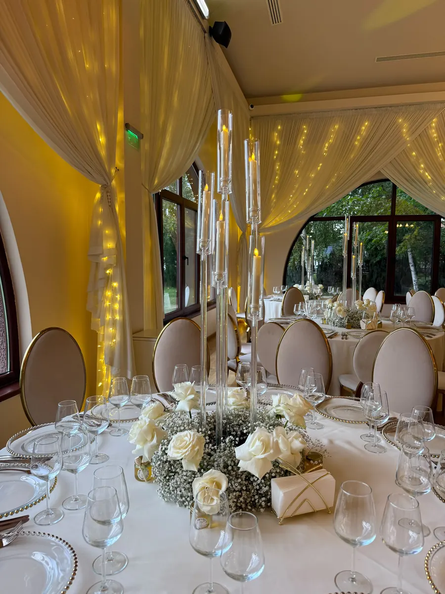 Masă rotundă cu coroană de gypsophila și trandafiri albi la baza candelabrului de cristal